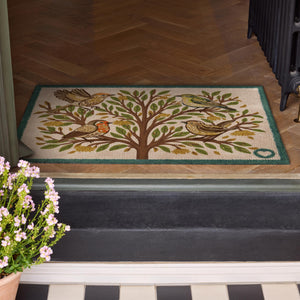 Chorus Bird Washable Doormat- a cotton doormat featuring multicoloured birds perched on a tree surround by orange and green leaves.