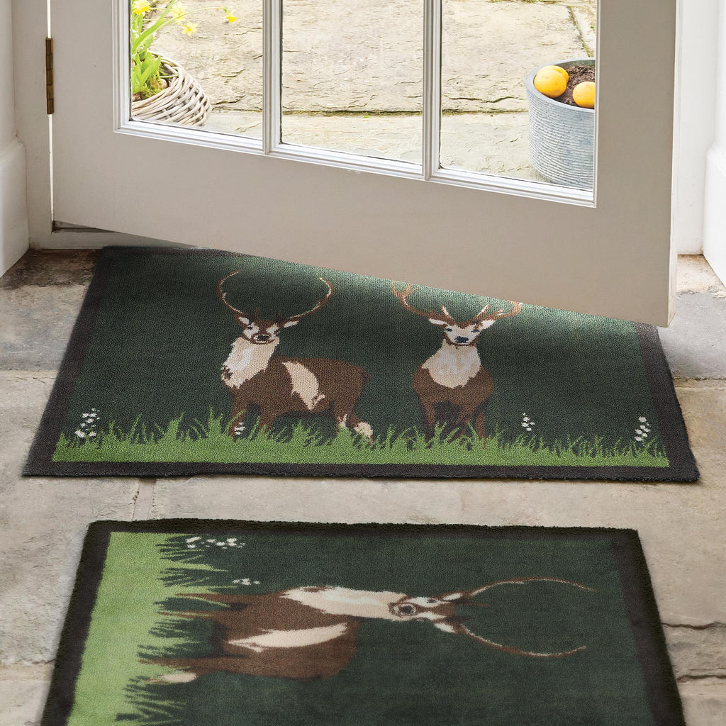 Green Deer Washable Doormat- a cotton doormat featuring two deers resting on green grass, surround by delicate white wildflowers.