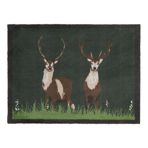 Green Deer Washable Doormat- a cotton doormat featuring two deers resting on green grass, surround by delicate white wildflowers.
