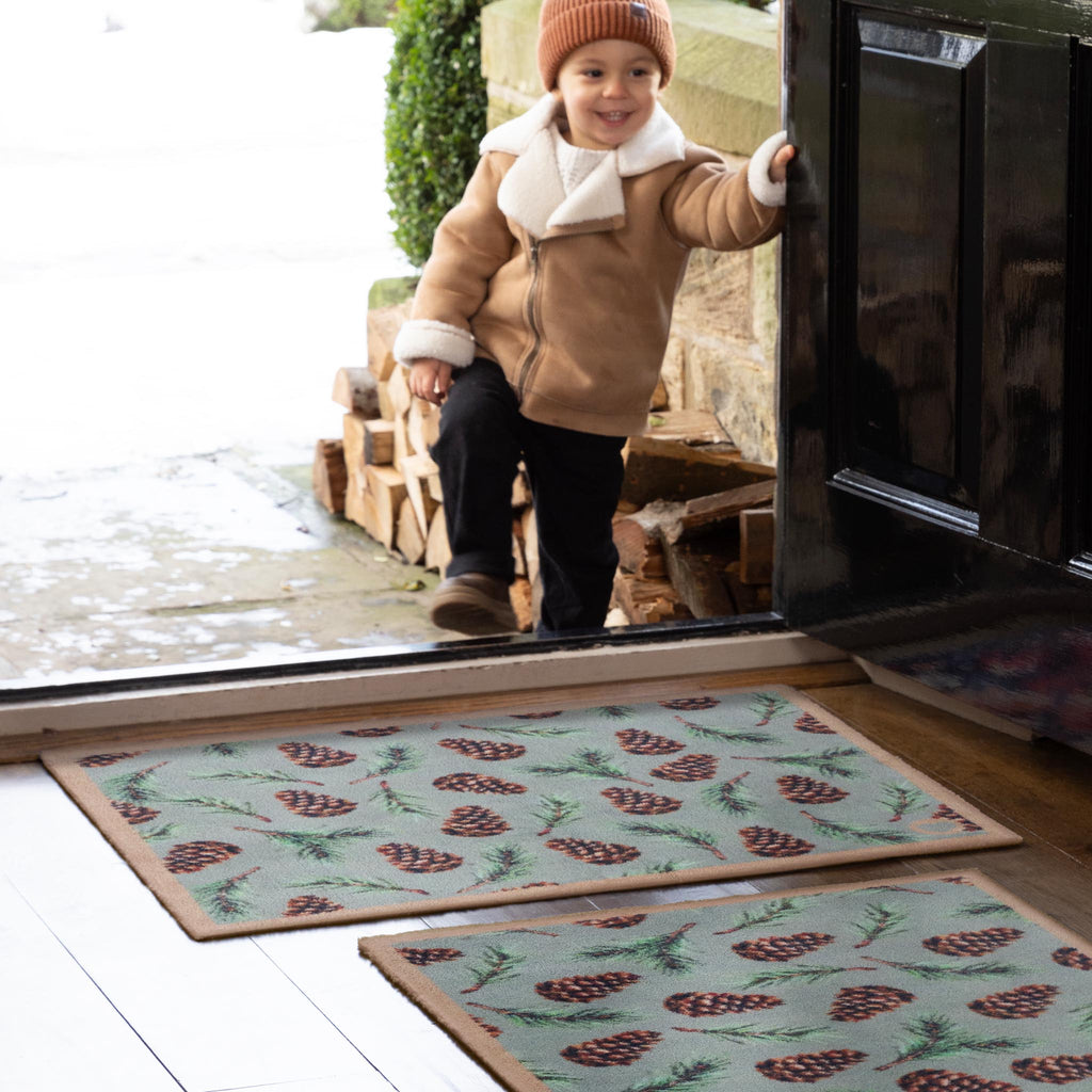 Pinecones Washable Doormat- a cotton doormat featuring scattered brown pinecones and green fern leaves.