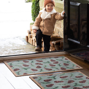 Pinecones Washable Doormat- a cotton doormat featuring scattered brown pinecones and green fern leaves.
