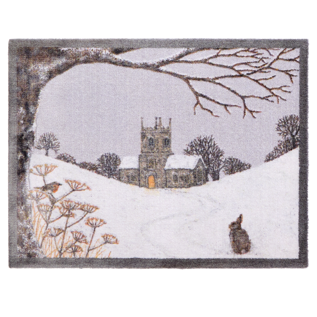 A rectangular doormat featuring a winter landscape scene with a snow-covered church, bare tree branches overhead, wildflowers in the foreground, and a rabbit near the bottom right, shown on a white background.
