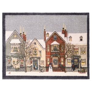 A rectangular doormat featuring a winter village scene with snow-covered houses, bare trees, storefronts, and a gray sky, finished with a dark border.