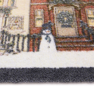 Close-up of a textured doormat featuring a winter city scene with a snowman standing in front of brick buildings.
