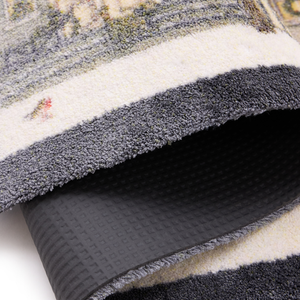 Close-up of a folded doormat showing a cream and gray patterned top, a dark charcoal pile edge, and a black textured underside.