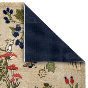A close-up of a patterned doormat with a corner folded back to show the dark textured underside. The top surface features a beige base with a whimsical woodland print including a mouse, red mushrooms, blue berries, and green leaves.