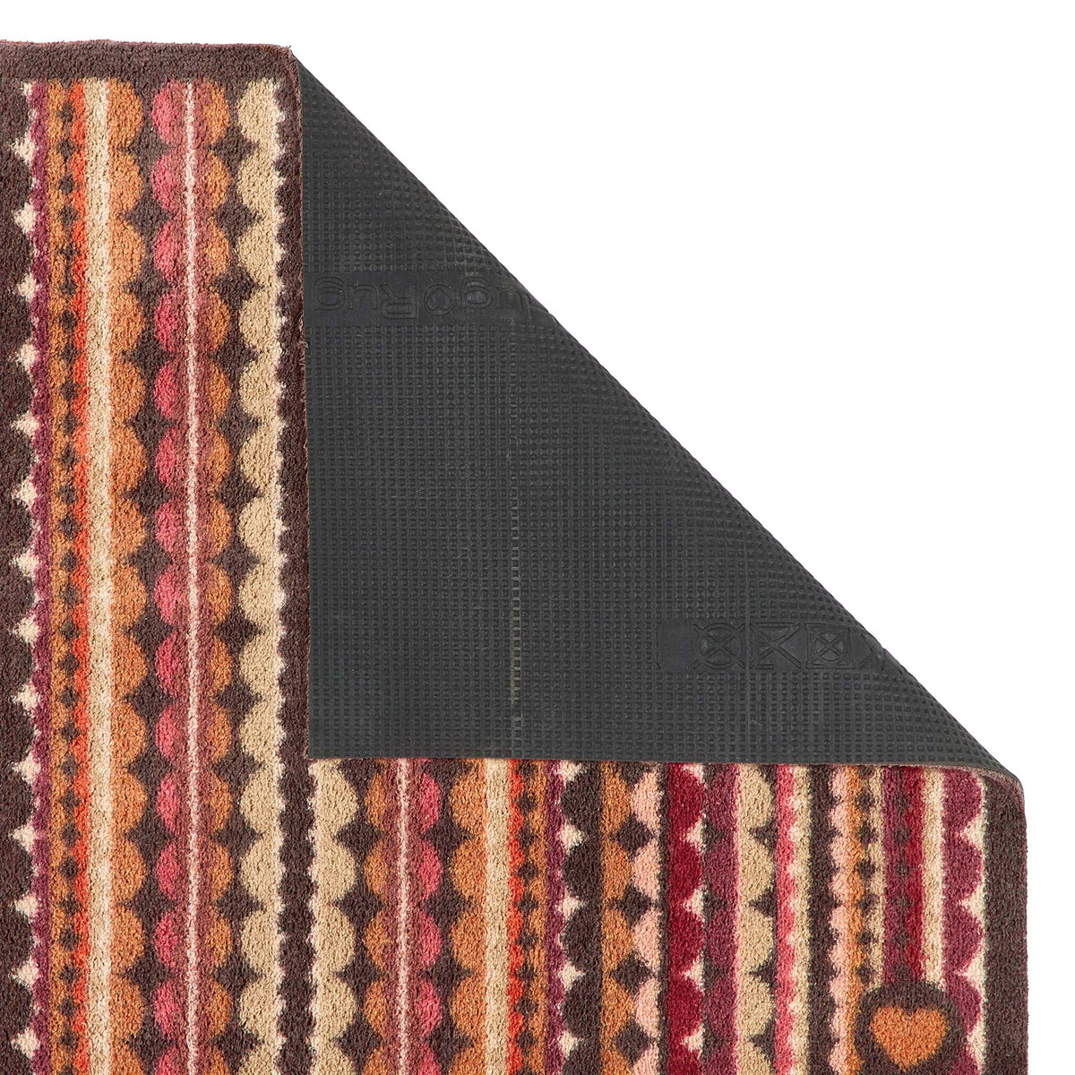 A close-up of a patterned doormat corner with one side folded back to show a dark textured backing, on a plain white background.