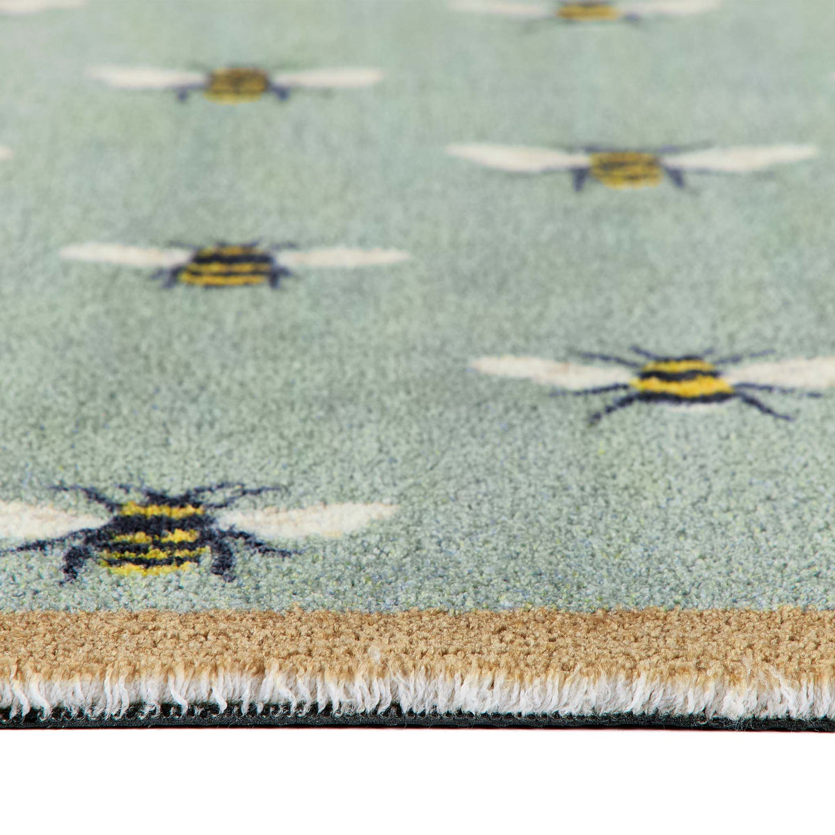 Close-up of a textured area doormat featuring a light sage green background with a repeating pattern of yellow and black bumblebees, finished with a beige and white fringed edge.