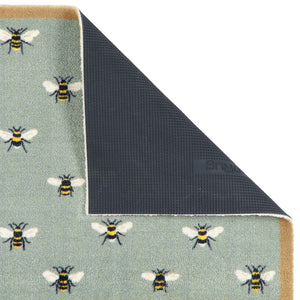 A close-up of a doormat corner with the top-left section folded back to show the backing. The visible top surface has a pale sage green base with a repeating pattern of bumblebees in black, yellow, and white.