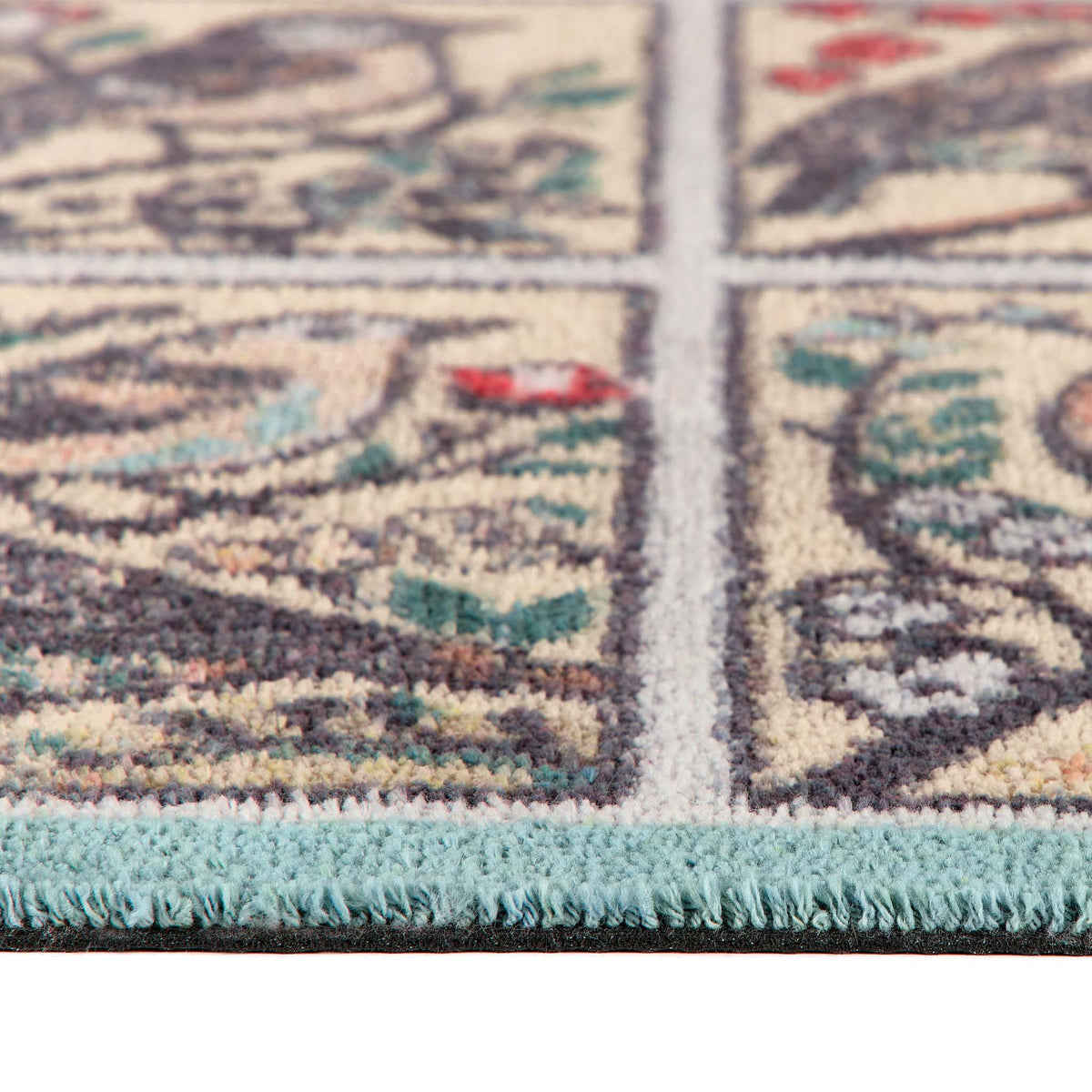 Close-up of a runner showing a cream background with a detailed multicolor floral pattern and a light blue fringed edge.