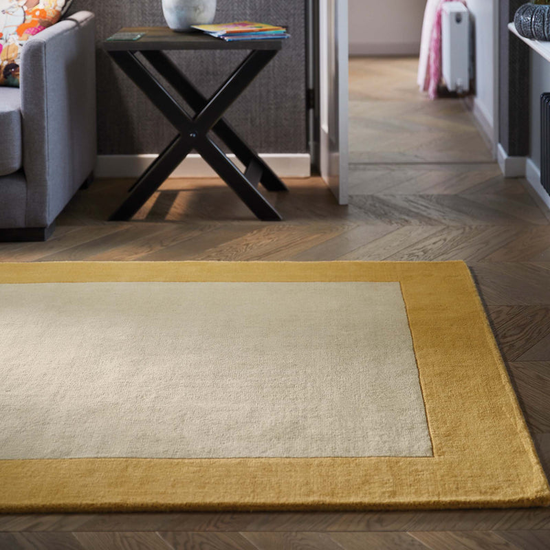 Borders Ochre Yellow 100% wool rug with a two-tone border design, styled in a  living room.