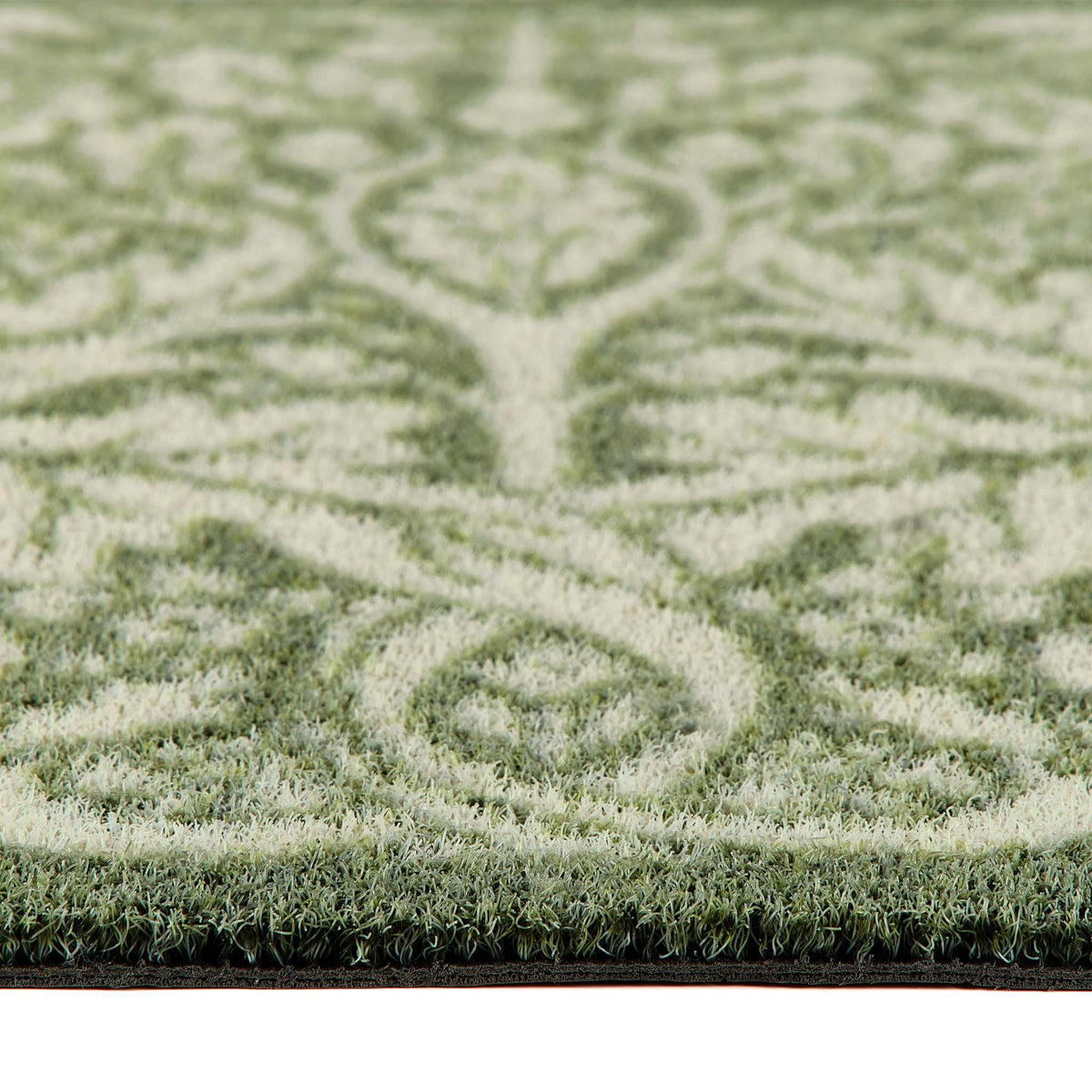 Close-up of a outdoor doormat  with a green and cream damask pattern, showing the pile height and the edge of the doormat. 