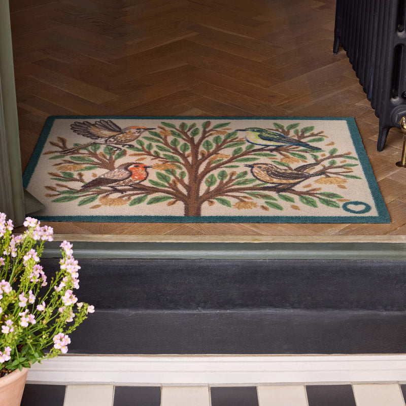 Chorus Birds Beige Charity Doormat with multicoloured birds on a tree, styled in a doorway.