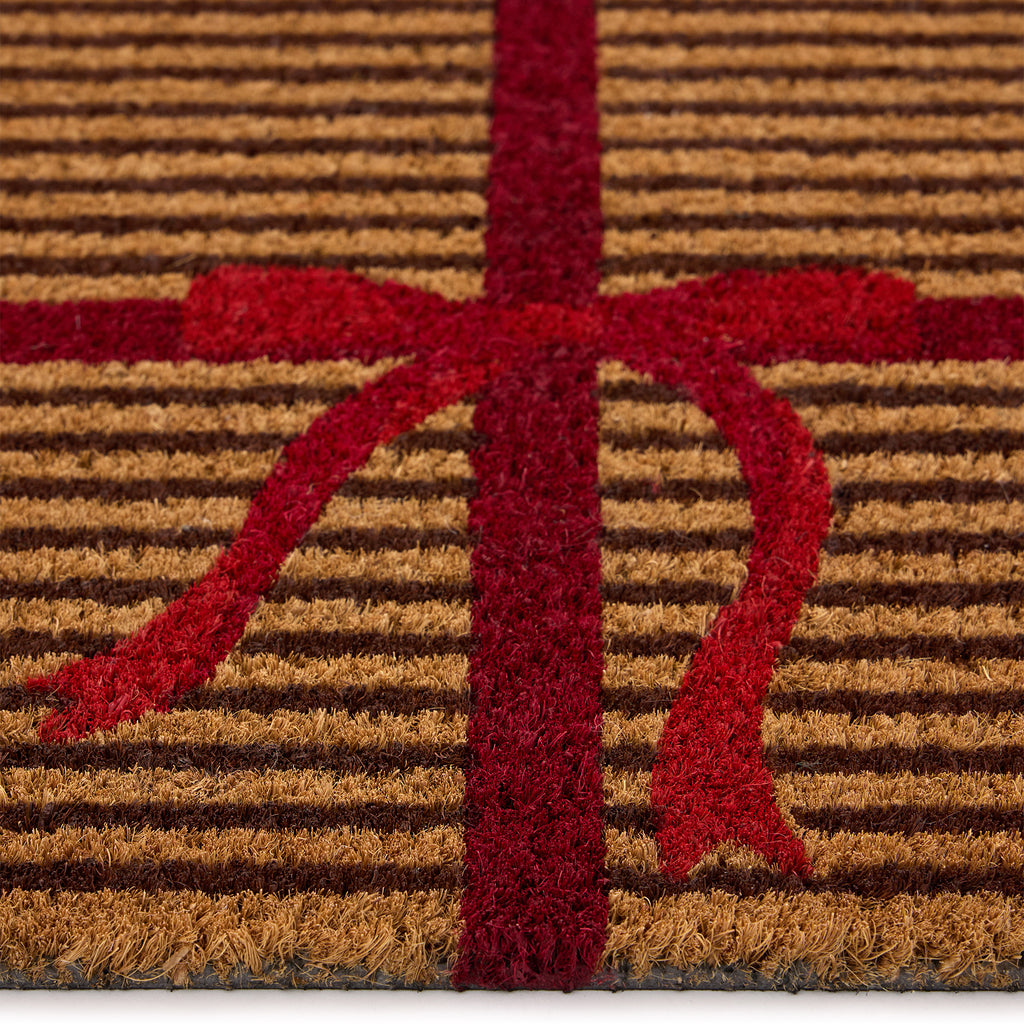 Discover the Christmas Gift Wrapped Coir Doormat- a coir doormat featuring a bright red bow and red lines giving the illusion of a present. 
