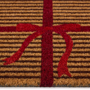 Discover the Christmas Gift Wrapped Coir Doormat- a coir doormat featuring a bright red bow and red lines giving the illusion of a present. 
