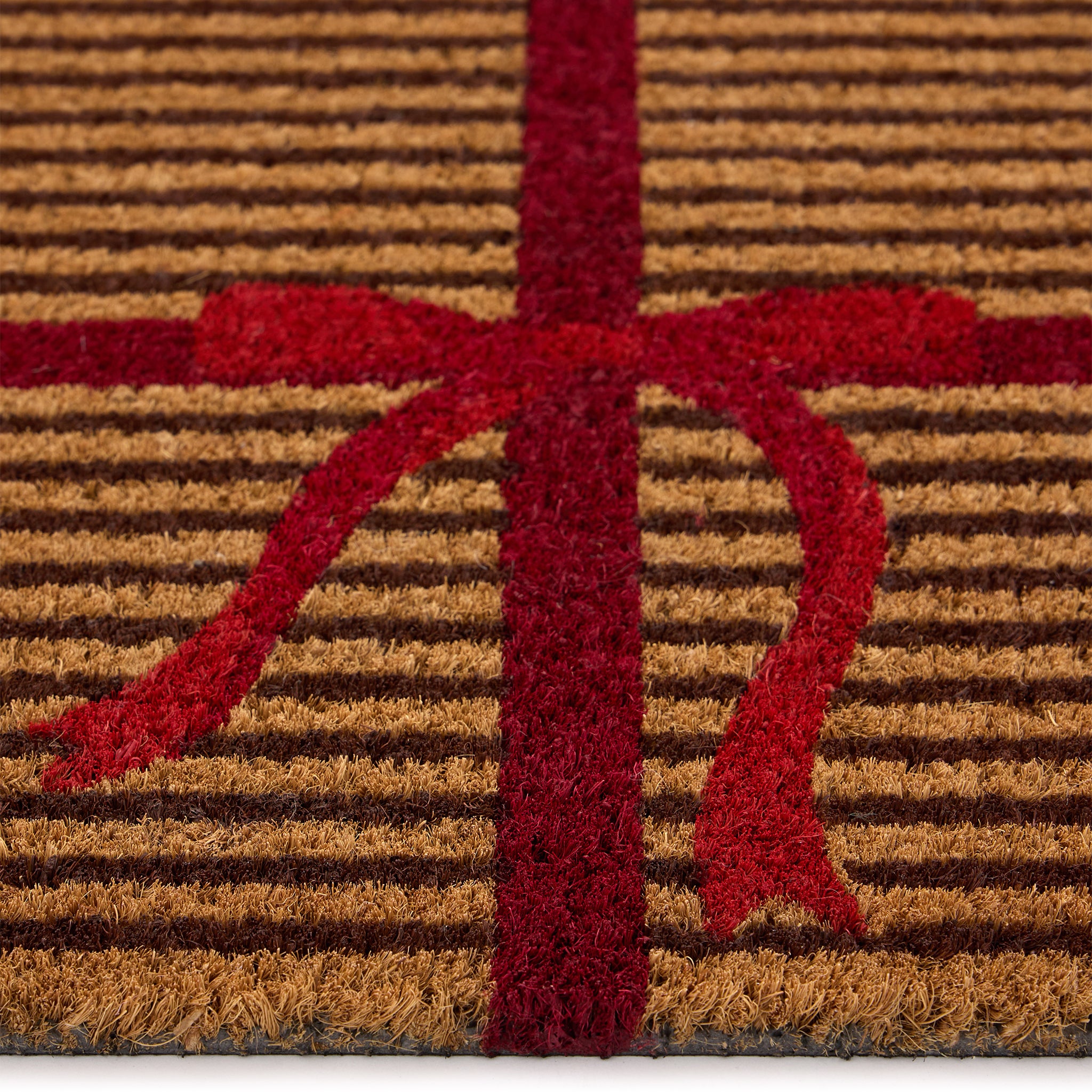 Discover the Christmas Gift Wrapped Coir Doormat- a coir doormat featuring a bright red bow and red lines giving the illusion of a present. 