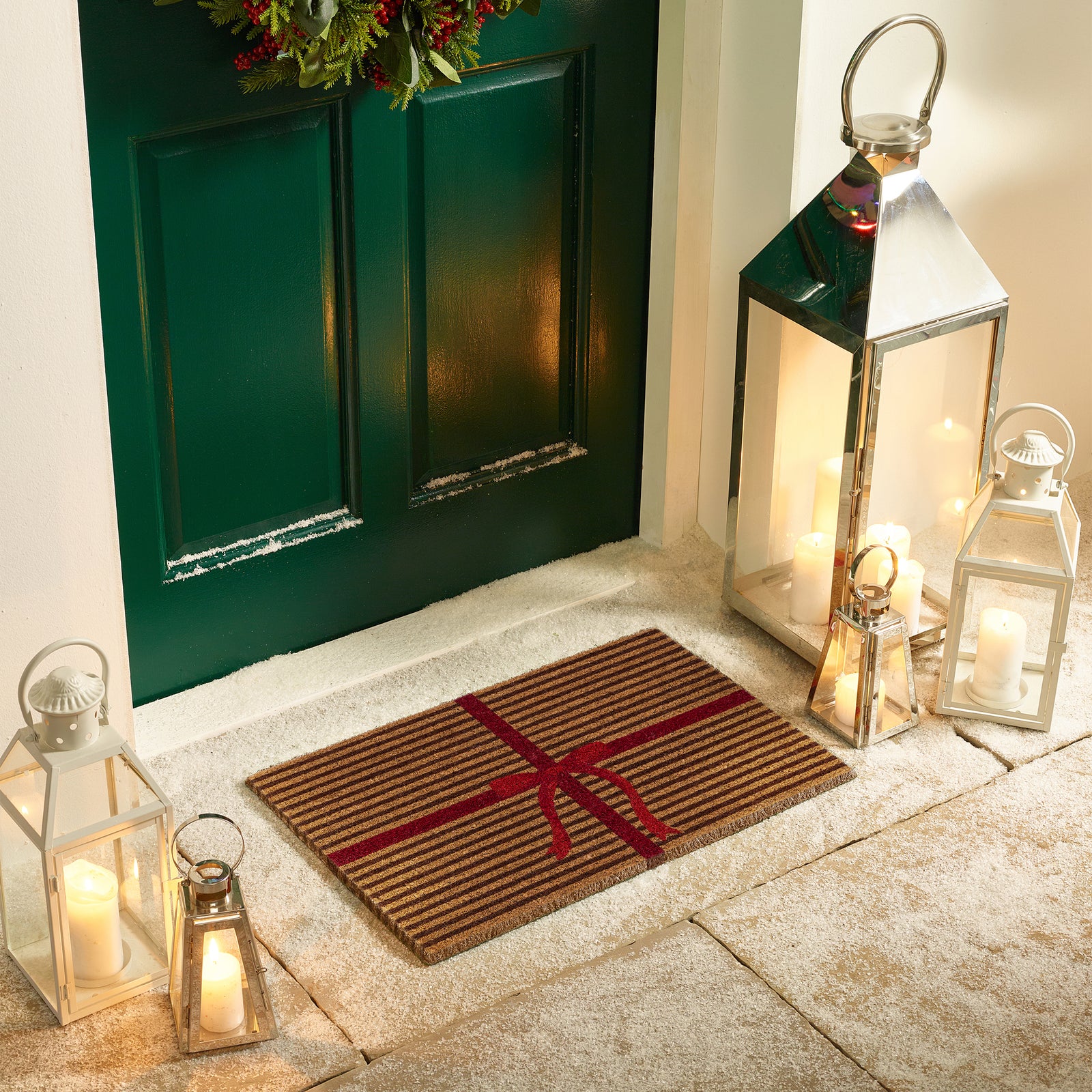 Discover the Christmas Gift Wrapped Coir Doormat- a coir doormat featuring a bright red bow and red lines giving the illusion of a present. 