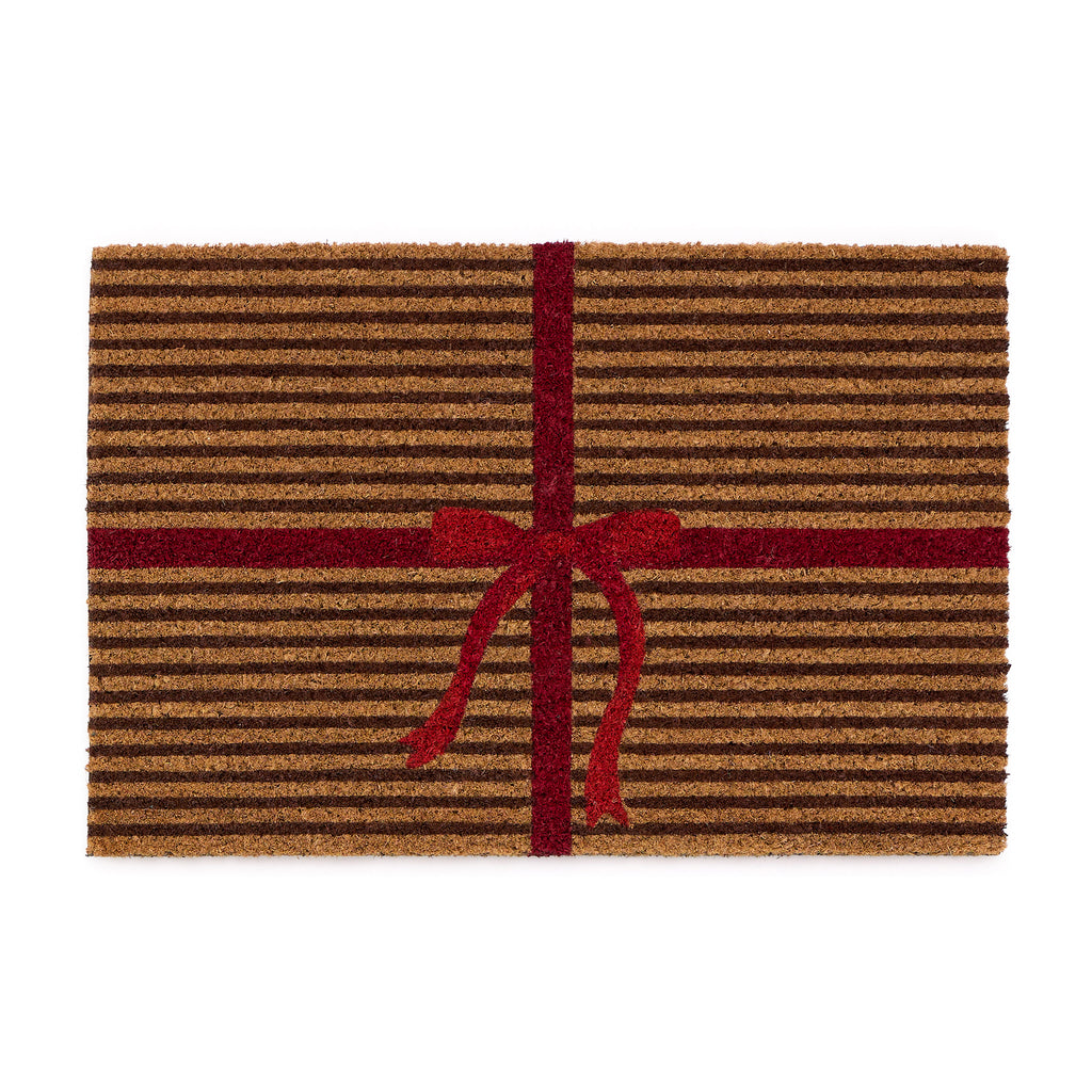 Discover the Christmas Gift Wrapped Coir Doormat- a coir doormat featuring a bright red bow and red lines giving the illusion of a present. 