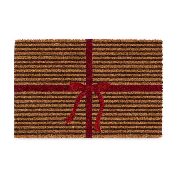 Discover the Christmas Gift Wrapped Coir Doormat- a coir doormat featuring a bright red bow and red lines giving the illusion of a present. 