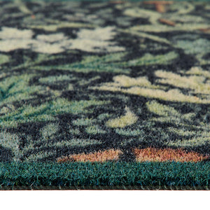 Close-up of a floral outdoor doormat with a dark green, black, and beige abstract floral pattern and a solid dark green shag border.