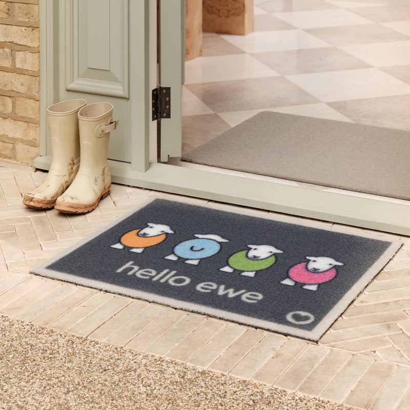 Hello Ewe Grey Outdoor Recycled Doormat with four colourful herdys, styled in a doorway.