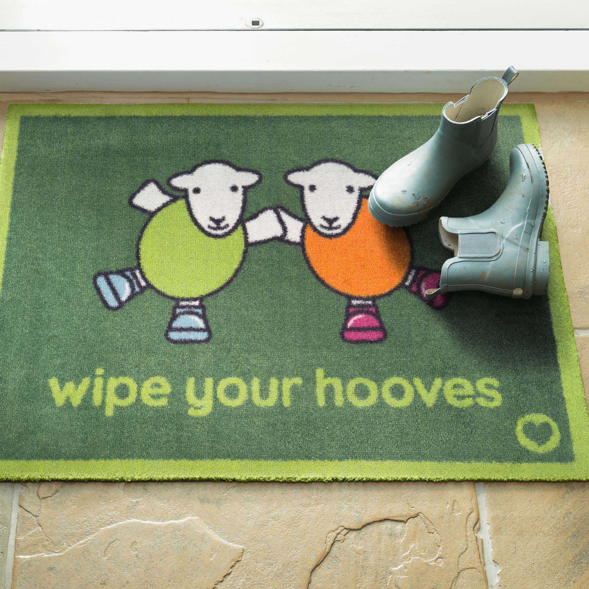 Herdy Wipe Your Hooves Green Doormat with a fun herdy design, styled in a doorway.