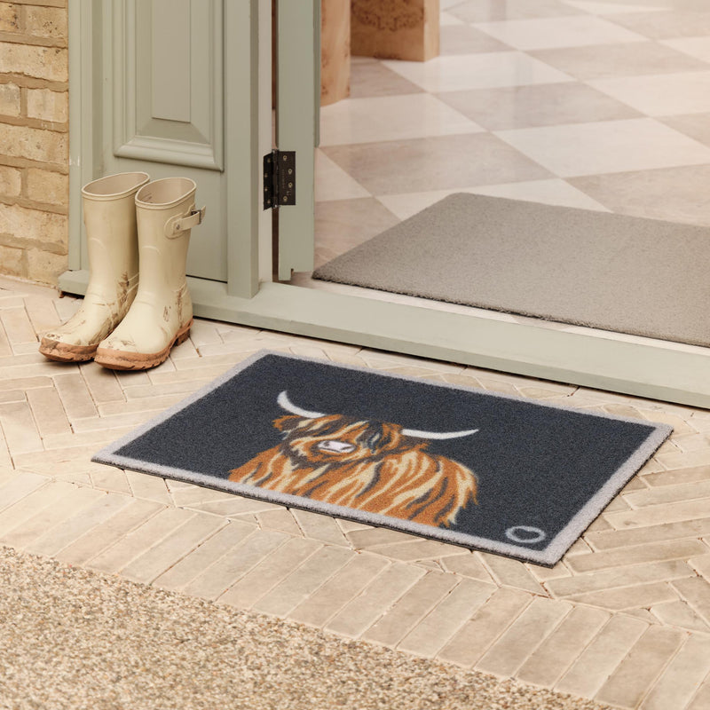 Highland Cow Blue Outdoor Doormat with a brown highland cow, styled in a doorway.