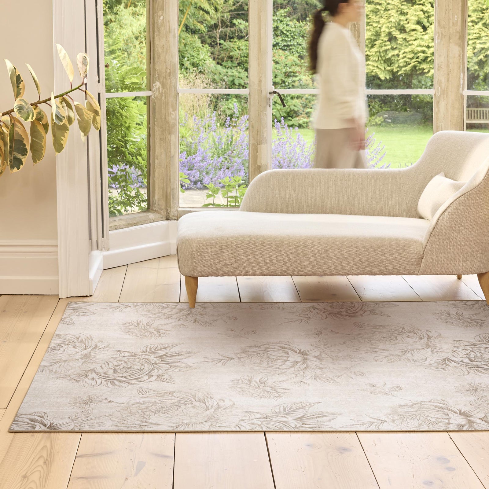 Living room with a beige sofa and decorative rug, featuring a blurred person and garden view.