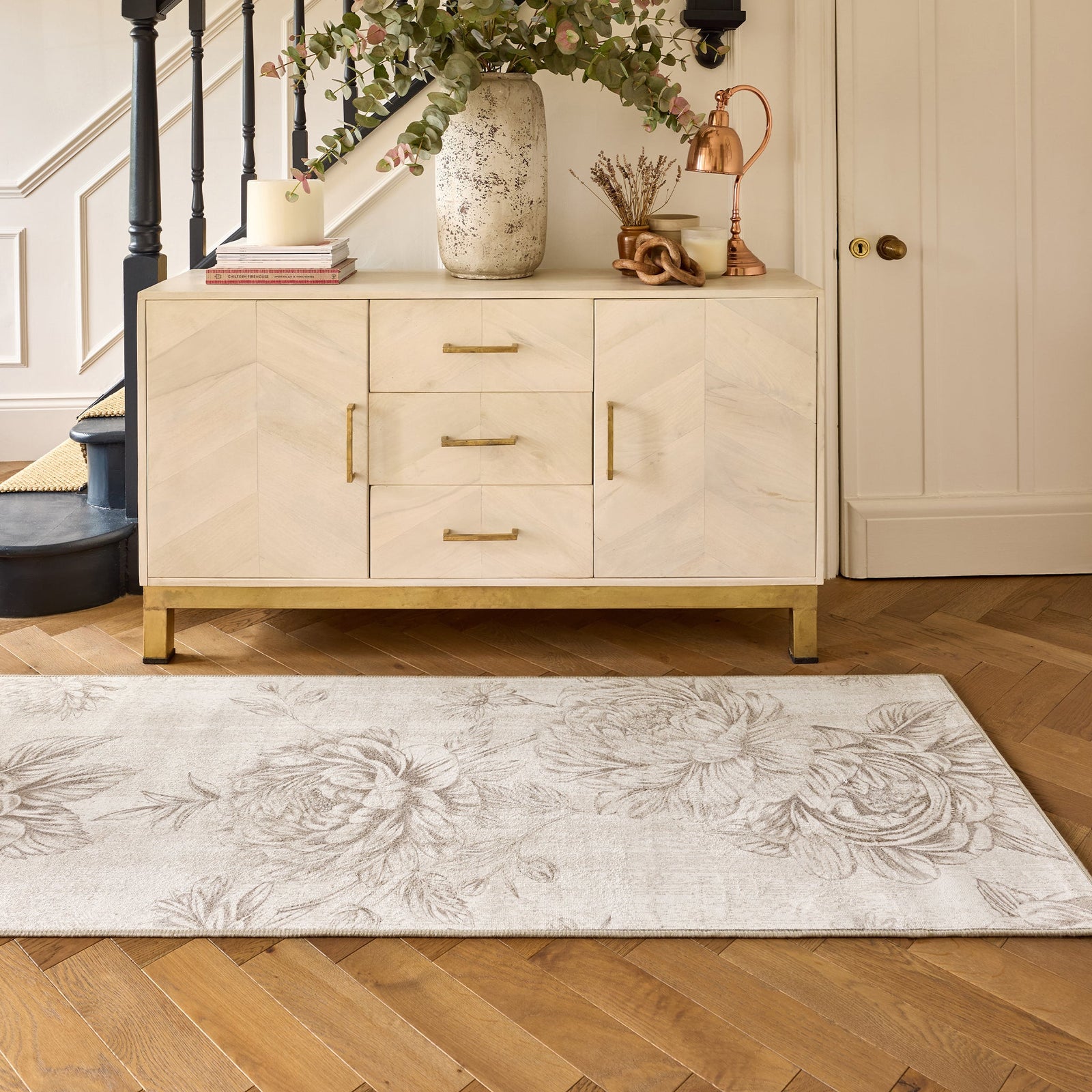 Hallway with a wooden floor featuring a stylish rug with a muted beige floral pattern and a cabinet in the background. 