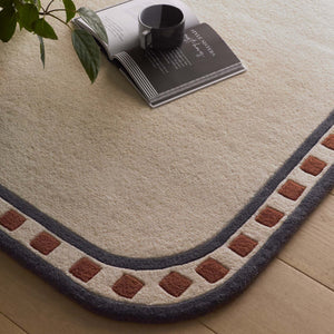 Borderline Natural Rug- a 100% wool cut pile rug featuring a brown and black geometric border. 