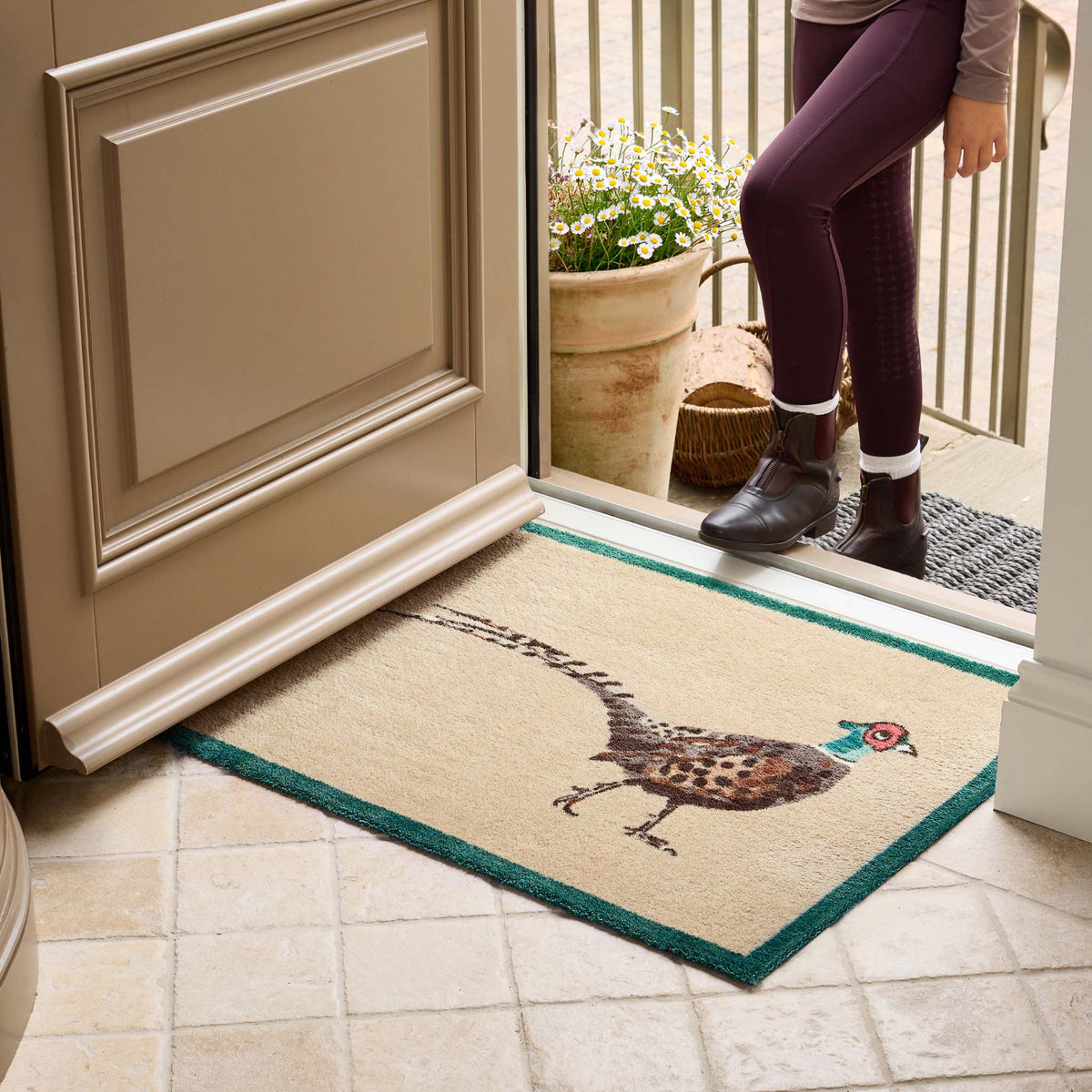 A rectangular entryway doormat with a pheasant illustration and teal border. 