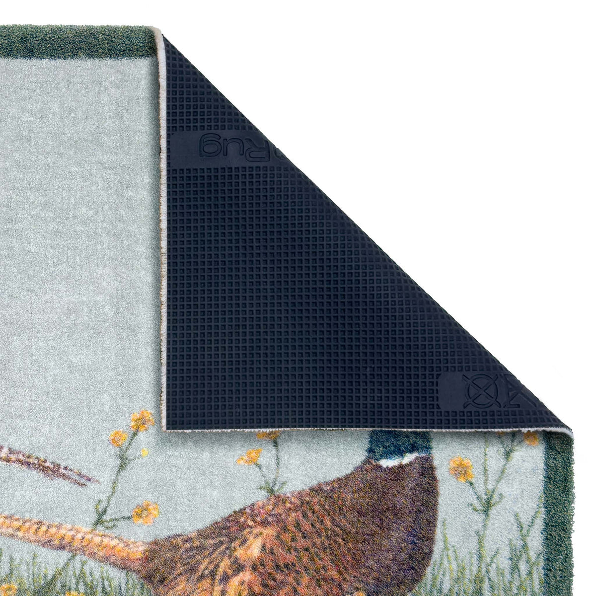 Close-up of a rug corner with one side folded back to show the dark textured backing, over a light gray background. The visible top surface shows a pheasant and wildflower pattern on a pale blue-gray field.
