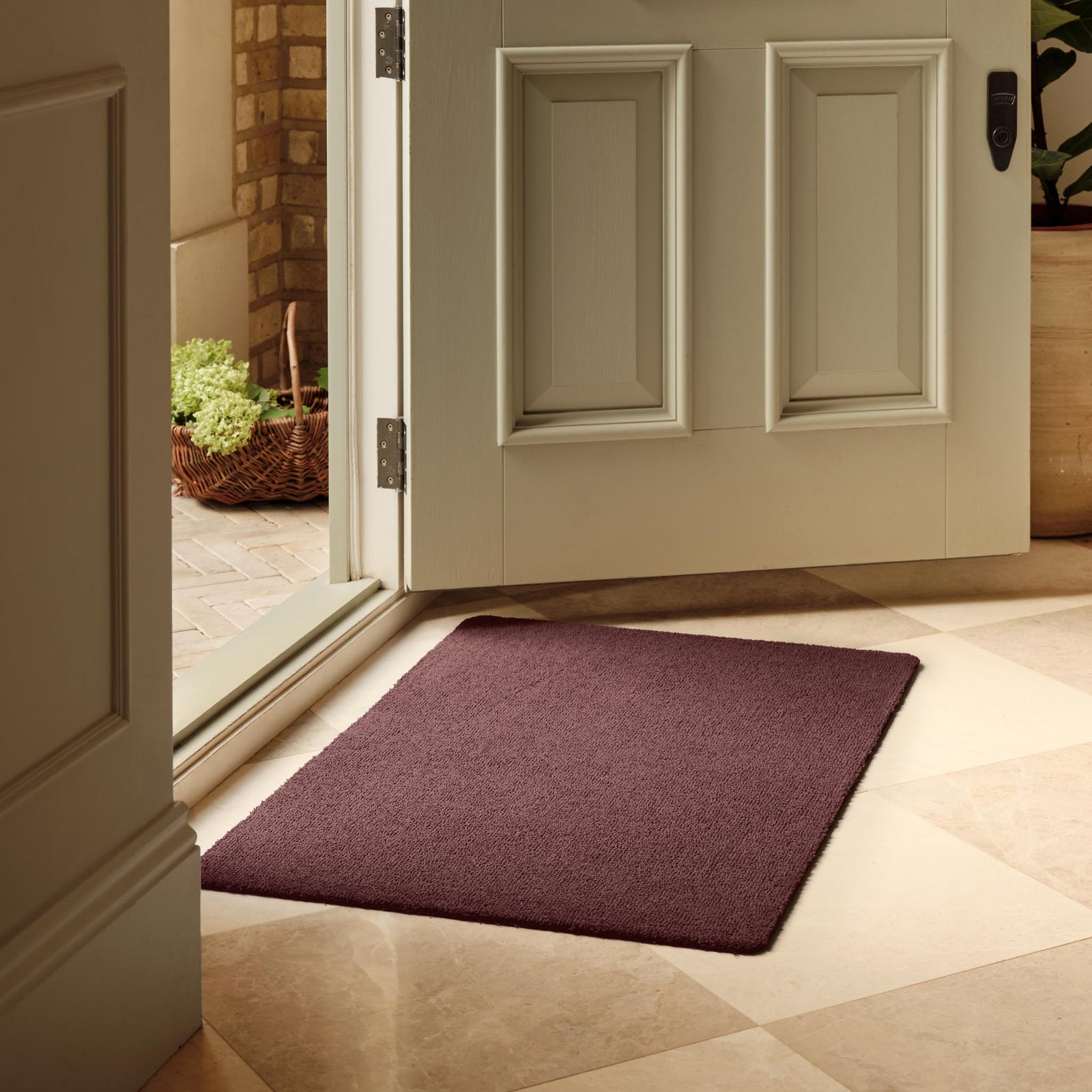 Sense Rose Pink Washable Doormat in a dark solid pink colour, styled in a doorway.