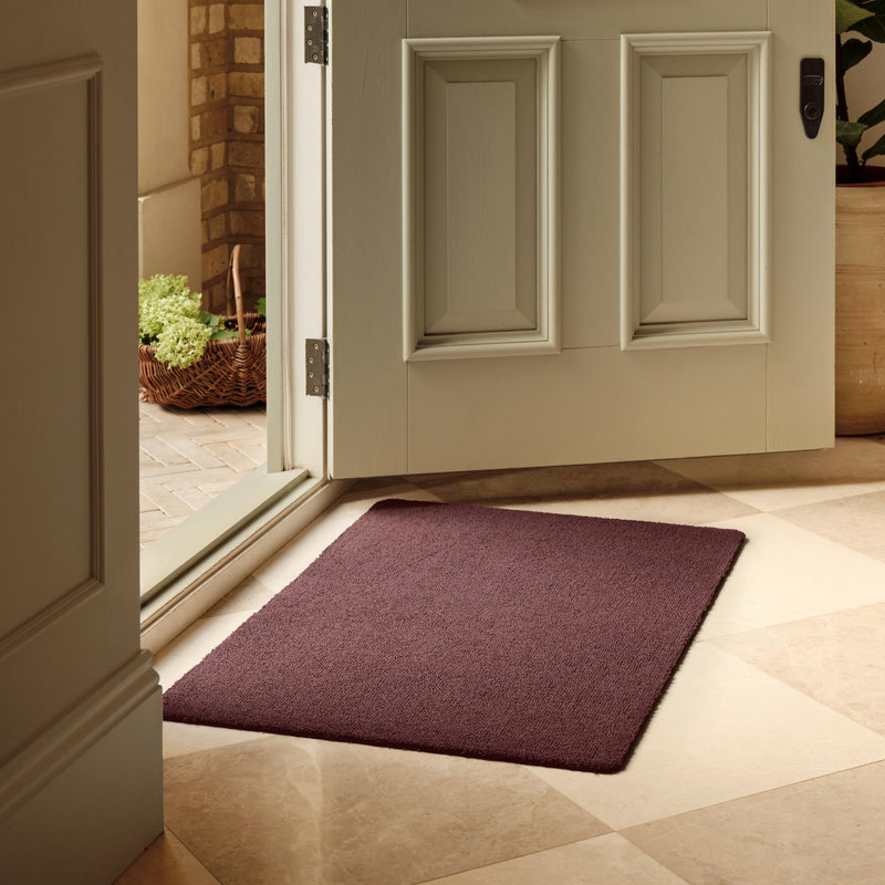 Sense Rose Pink Washable Doormat in a dark solid pink colour, styled in a doorway.