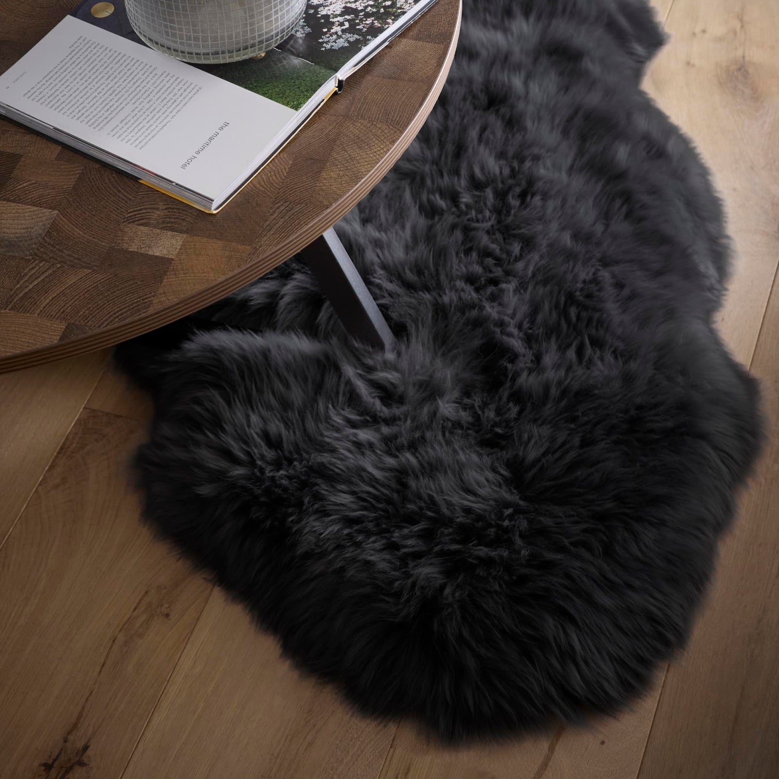 Close-up of Double Sheepskin Black Rug made up of long-haired wool, styled on wooden flooring.