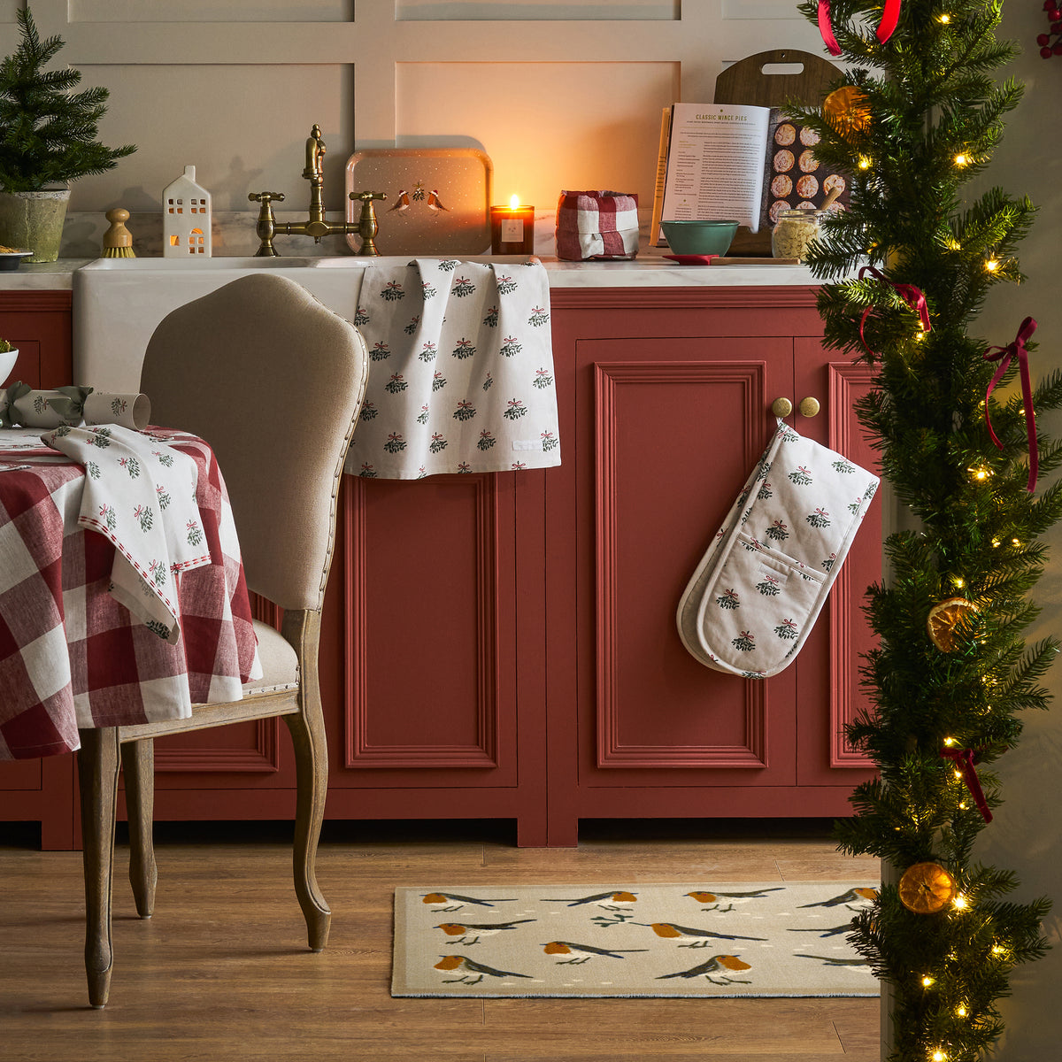 A doormat with a robin design and a cream background, placed in a kitchen surrounded by kitchen ornaments and kitchen textiles. 