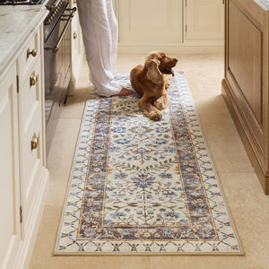 A long rectangular area rug with an ornate traditional floral pattern in cream, beige, muted blue, and olive green, shown flat against a solid white background.