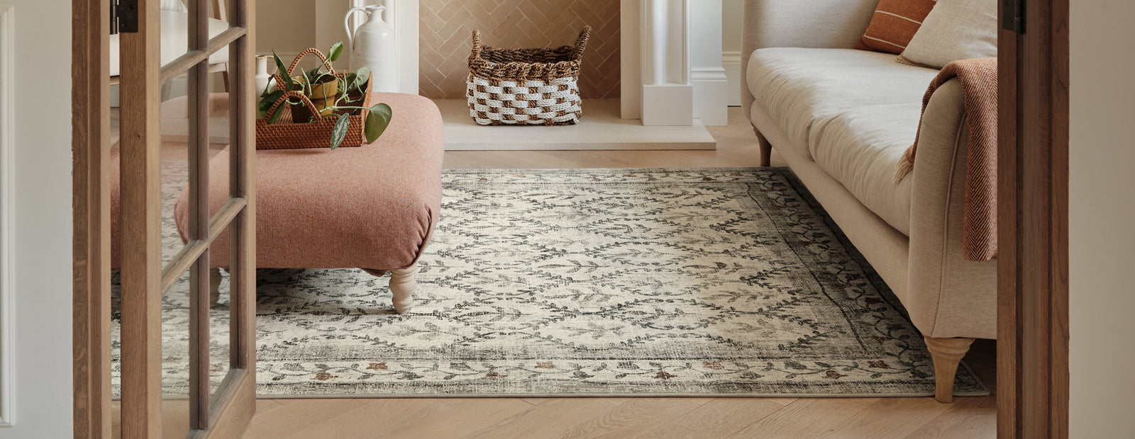 A rug with a distressed, vintage-style pattern in beige, brown, and grey, shown in a cozy living room setting viewed through open wooden doors.