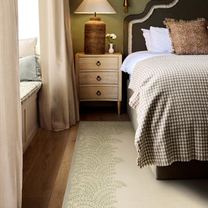 Whispering Fern Parchment Eco-Washable Rug with a fern leaf border design, styled under a bed. 