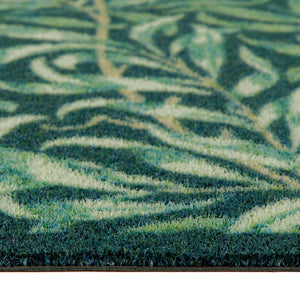 Close-up of a textured outdoor doormat with a leafy pattern in shades of green, teal, and cream.