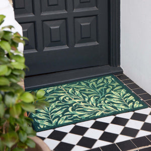 A rectangular green outdoor doormat with a leafy vine pattern, placed in front of a black paneled front door on a tiled porch.